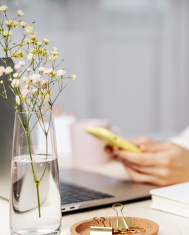 Pinterest - Frau mit Handy in der Hand, gelb, sitzt am Tisch , darauf Blumen und Laptop